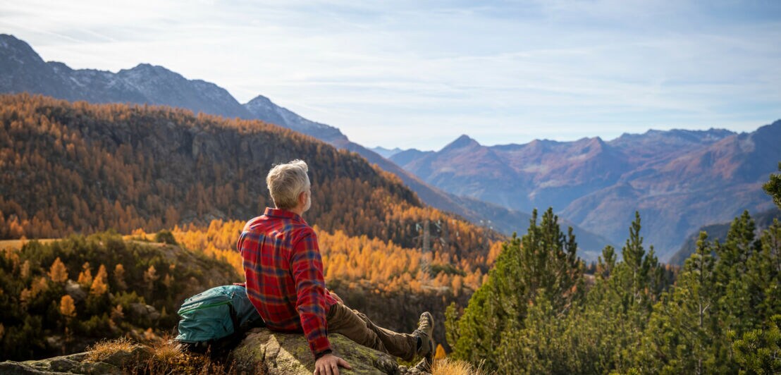 Ein Mann sitzt auf einem Berg und blickt auf farbenprächtige Bäume.