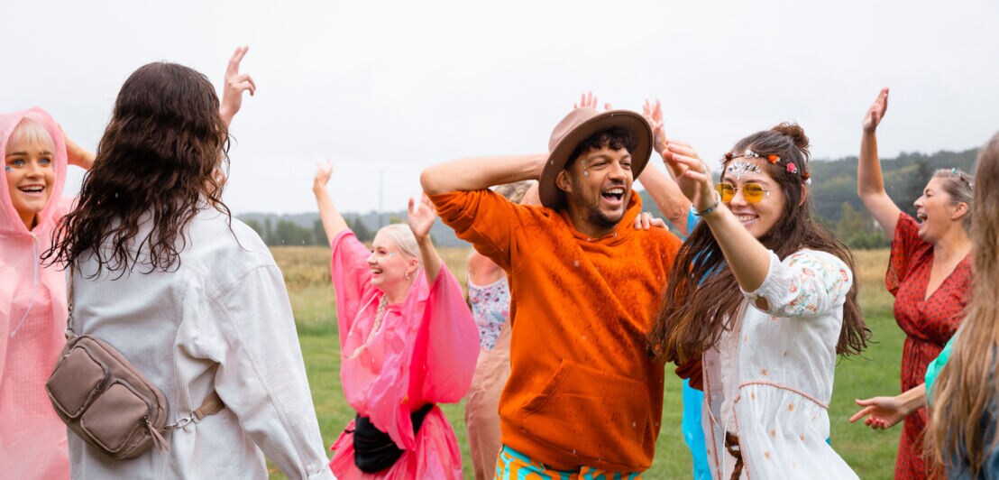 Menschen tanzen im Regen, manche tragen einen Regenponcho.