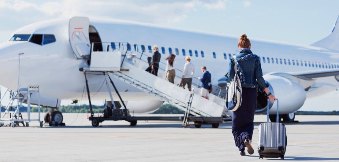 Personen in Reihe mit Handgepäck auf dem Rollfeld beim Boarding.