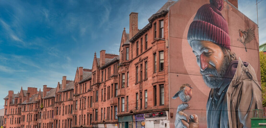 Rotes Backsteingebäude mit Wandgemälde eines Mannes mit roter Mütze und Spatz auf der Hand.