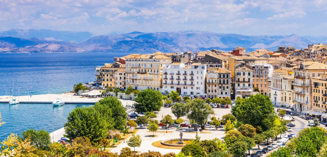 Küstenstadt mit historischen Gebäuden, Blick auf das blaue Meer und Berge im Hintergrund unter bewölktem Himmel