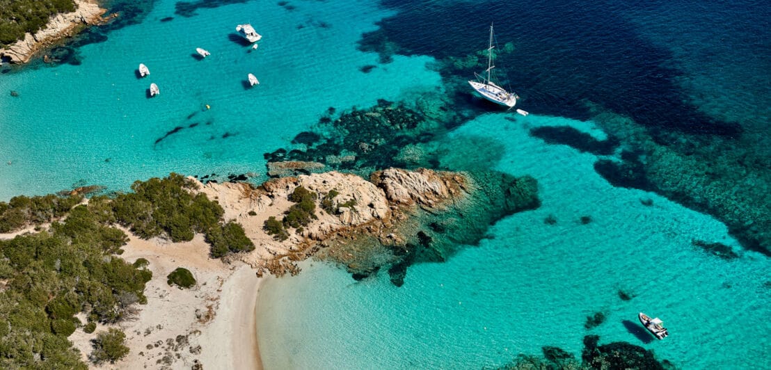 Aufsicht einer flachen Felsküste mit feinen Sandstränden an türkisblauem Meer mit Motorbooten.