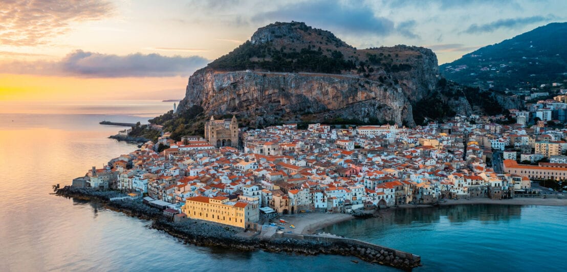 Mediterrane Stadt am Meer am Fuße eines Felsens mit Abendlicht.