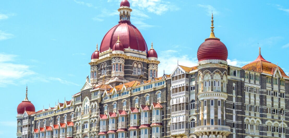 Historisches Hotel Taj Mahal Palace in Mumbai mit roten Kuppeln und detailreicher Fassade unter blauem Himmel.