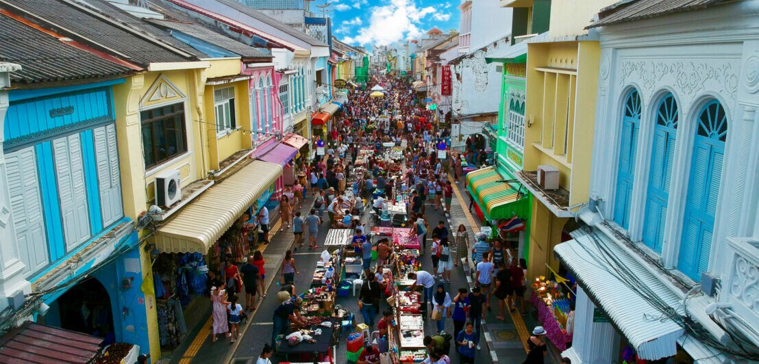 Schmale Straße im Stadtzentrum mit Markttreiben zwischen bunten Hausfassaden.