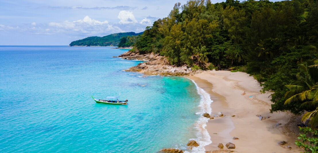 Kleine Meeresbucht mit einem Fischerboot im türkisblauen Wasser an einem Sandstrand, umgeben von tropischem Regenwald.