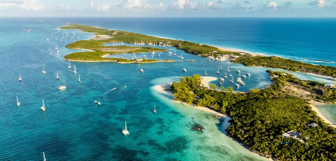 Begrünte Inselgruppe mit Sandstränden, umgeben von türkisblauem Meer mit etlichen Segelboten.