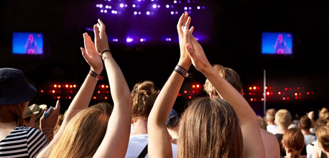Zwei Personen applaudieren mit hoch erhobenen Armen während eines Konzerts auf dem Roskilde Festival. 