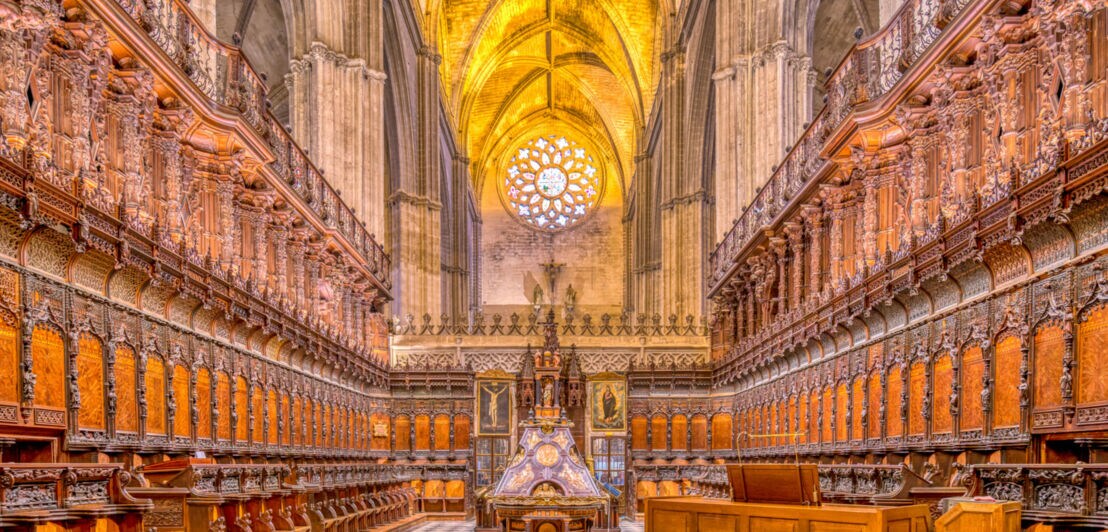 Innenraum einer gotischen Kathedrale mit reich verzierten Holzsitzreihen und gewölbten Deckenbogen mit goldener Beleuchtung