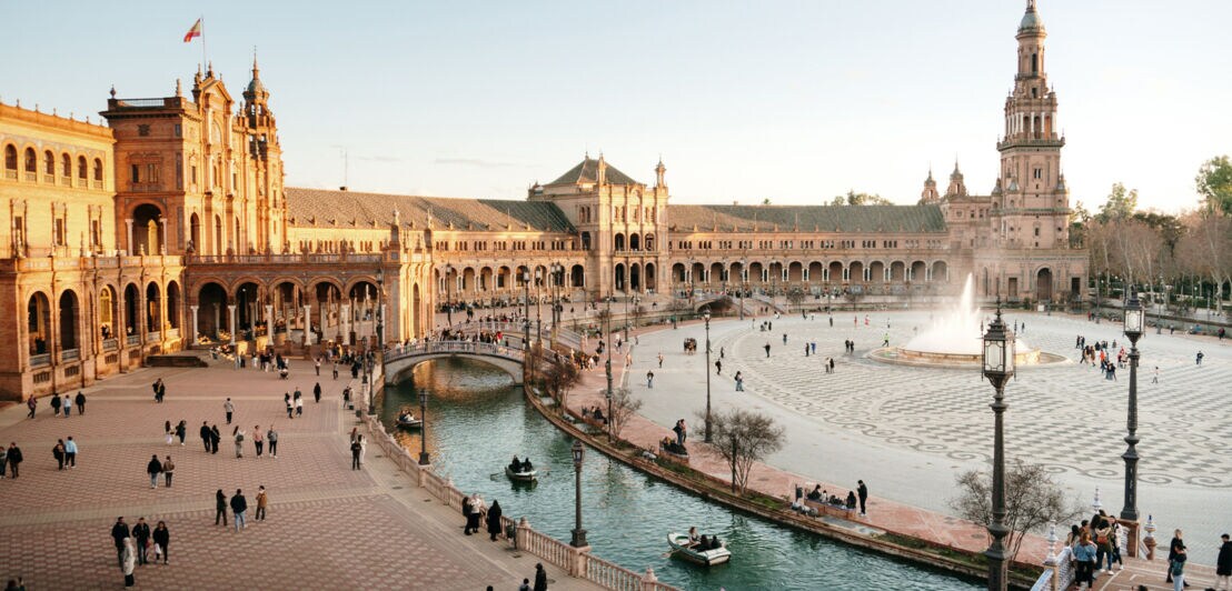 Plaza de España in Sevilla mit halbkreisförmigem Gebäude, Brücke über Kanal und zentralem Springbrunnen bei Tageslicht