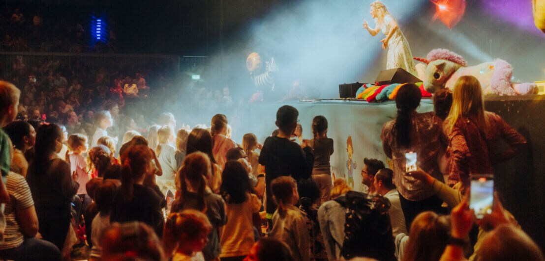 Simone Sommerland steht am Rand der Bühne, viele Kinder schauen ihr aus dem Publikum gebannt zu.