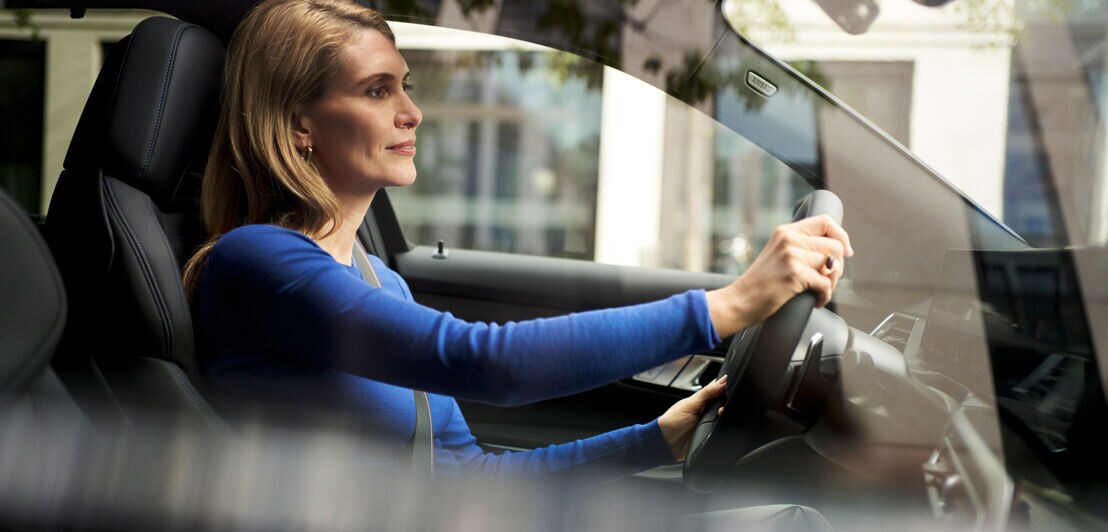 Eine Frau mit blauem Oberteil am Steuer eines BMW auf der Straße.