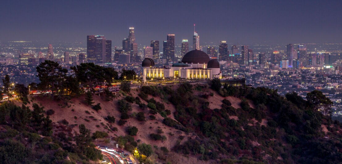 Beleuchtete Sternwarte auf einem Hügel vor der Skyline von Los Angeles bei Nacht.