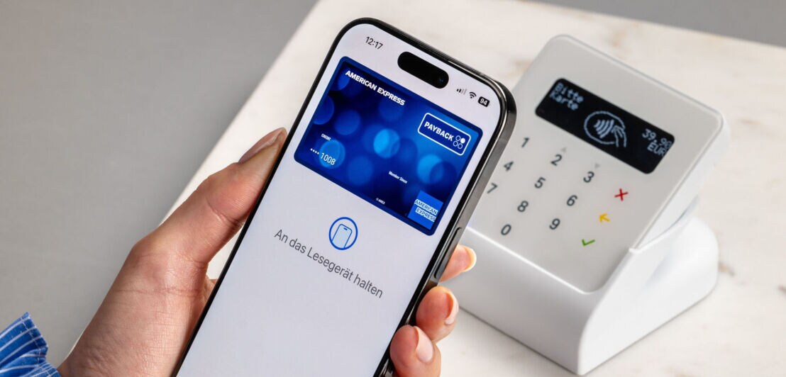 Eine Person hält ihr Smartphone mit der hinterlegten American Express PAYBACK Kreditkarte vor ein Kartenlesegerät.