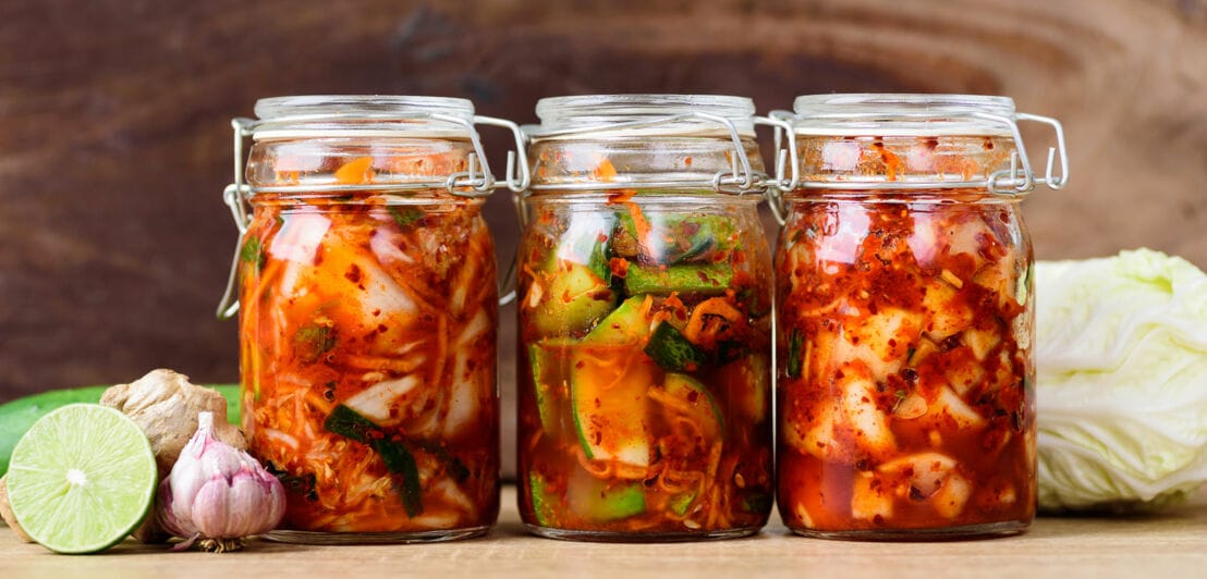 Drei Einmachgläser nebeneinander mit fermentiertem Chinakohl mit roter Gewürzpaste und Gemüse.