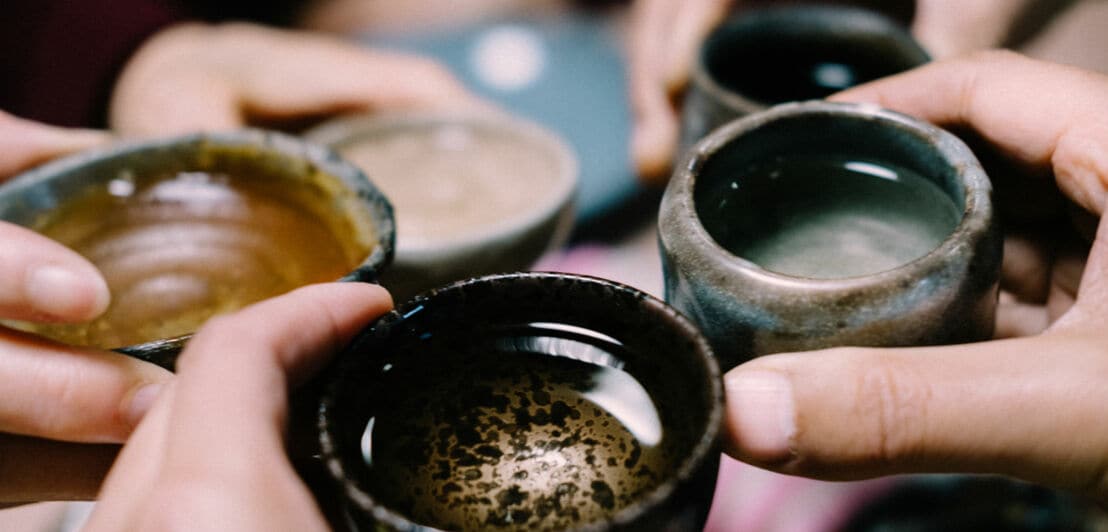 Mehrere Hände halten kleine Tassen aus Keramik und stoßen an.