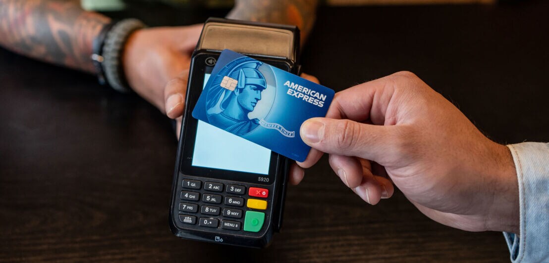 Kontaktlose Zahlung mit einer blauem American Express Kreditkarte an einem Kartenlesegerät.
