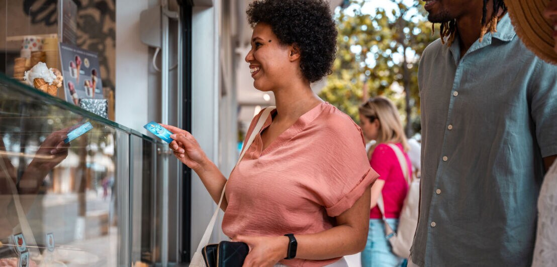 Eine Frau bezahlt mit einer blauen American Express Kreditkarte an der Theke einer Eisdiele mit Straßenverkauf.