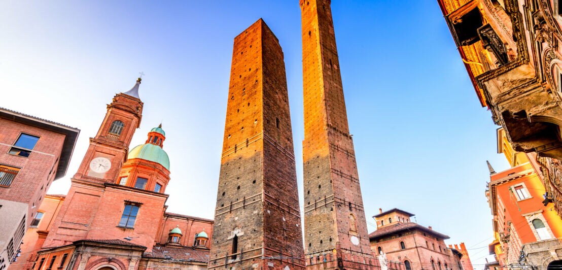 Zwei mittelalterliche schiefe Türme in Bologna, Italien, umgeben von historischen Gebäuden bei klarem Himmel