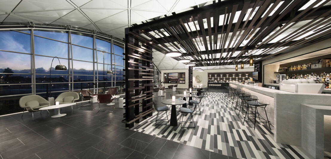 Menschenleere, moderne Flughafenlounge mit Barbereich und Panoramablick aufs Rollfeld am Abend.