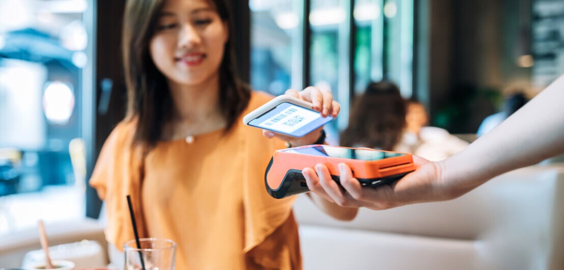 Eine Frau bezahlt mit ihrem Smartphone per App an einem Kartenlesegerät in einem Restaurant.