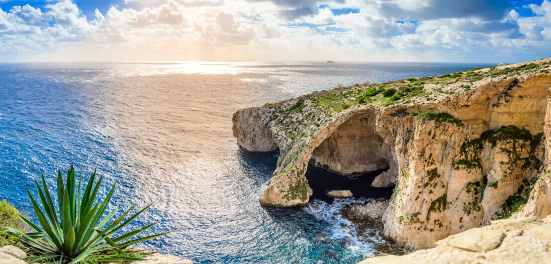 Felsformation mit natürlichem Bogen über blauem Meer unter bewölktem Himmel bei Sonnenuntergang.