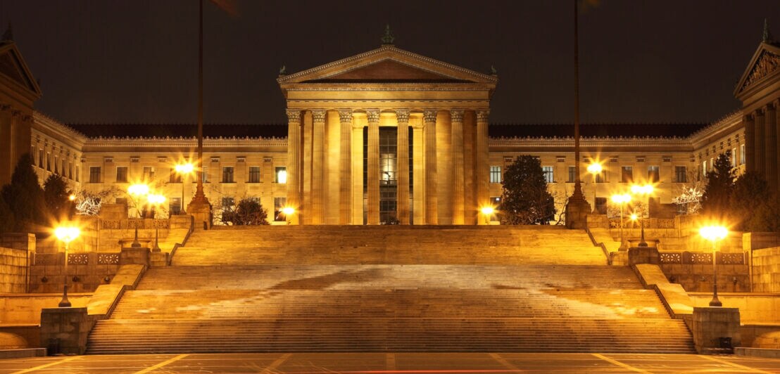 Beleuchtetes klassizistisches Gebäude mit breiter Treppe bei Nacht