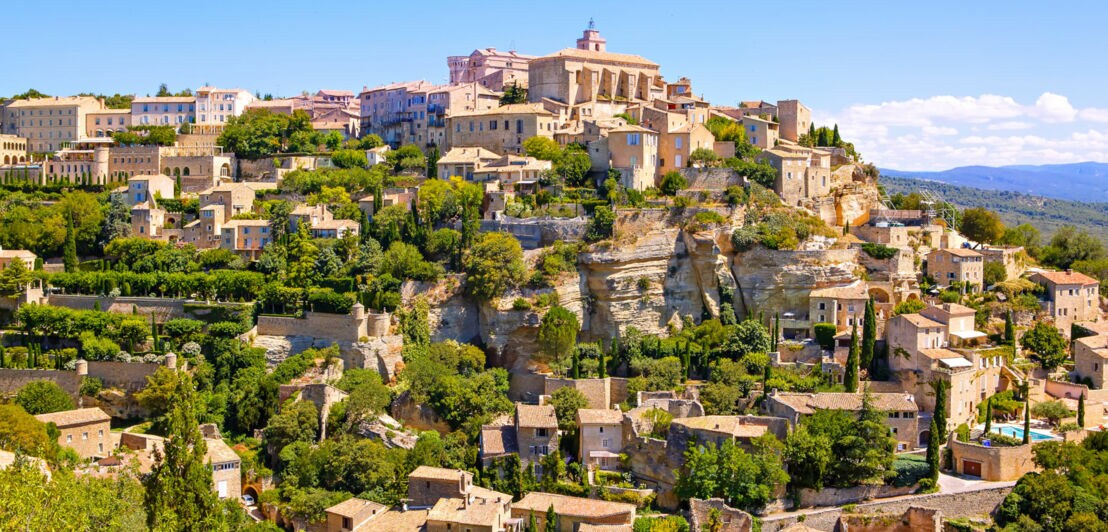 Historisches Dorf mit Steinhäusern und grünen Gärten auf einem Hügel unter blauem Himmel
