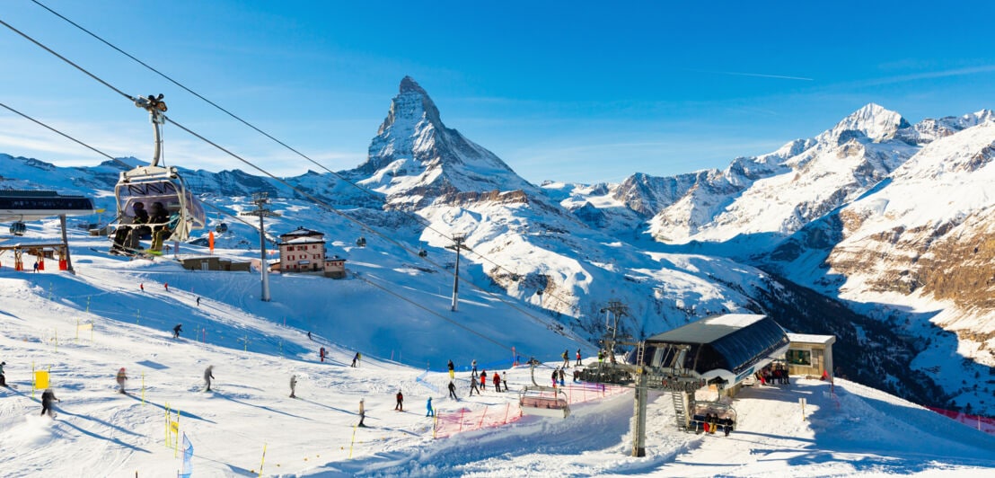 Skigebiet mit Seilbahn und Skifahrern vor schneebedecktem Matterhorn unter klarem blauem Himmel