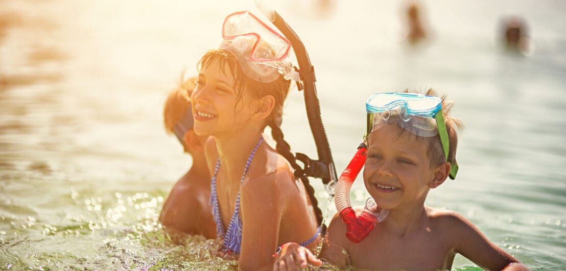 Lachende Kinder mit Schnorchelausrüstung spielen im Wasser bei Sonnenlicht
