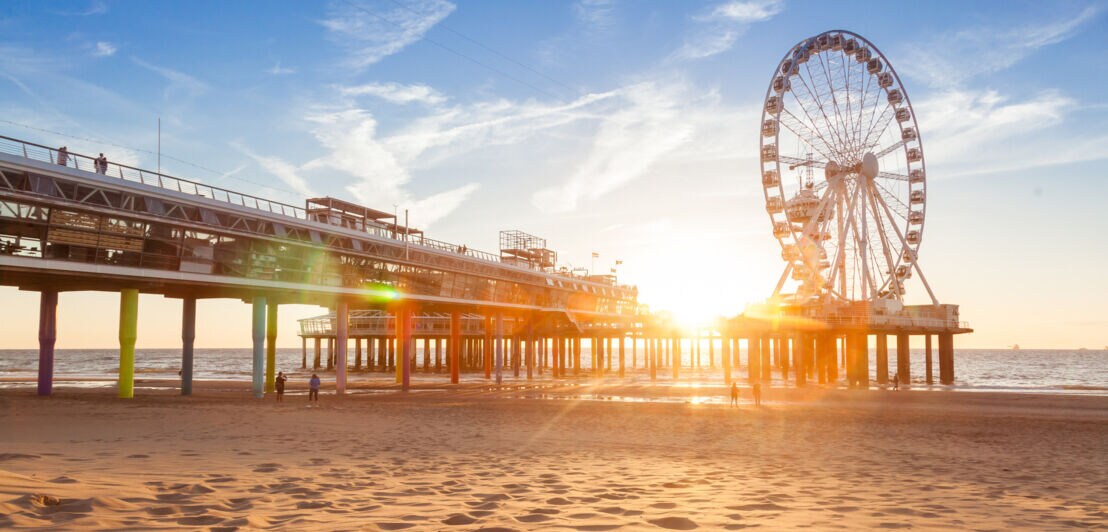 Sonnenuntergang am Strand mit einem Pier und einem großen Riesenrad am Meer.