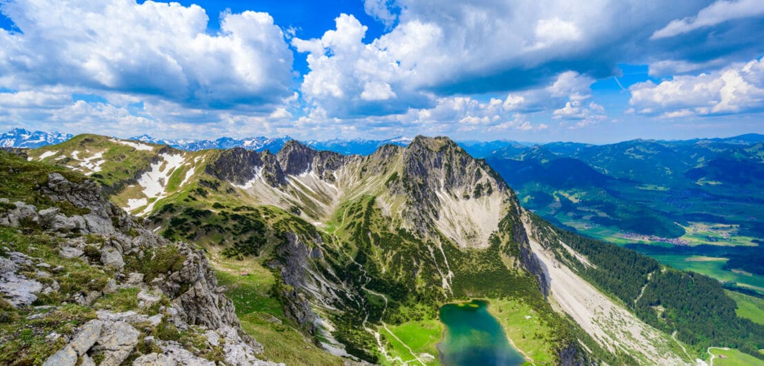Luftaufnahme eines blaugrünen Bergsees unterhalb eines schroffen Gipfels.