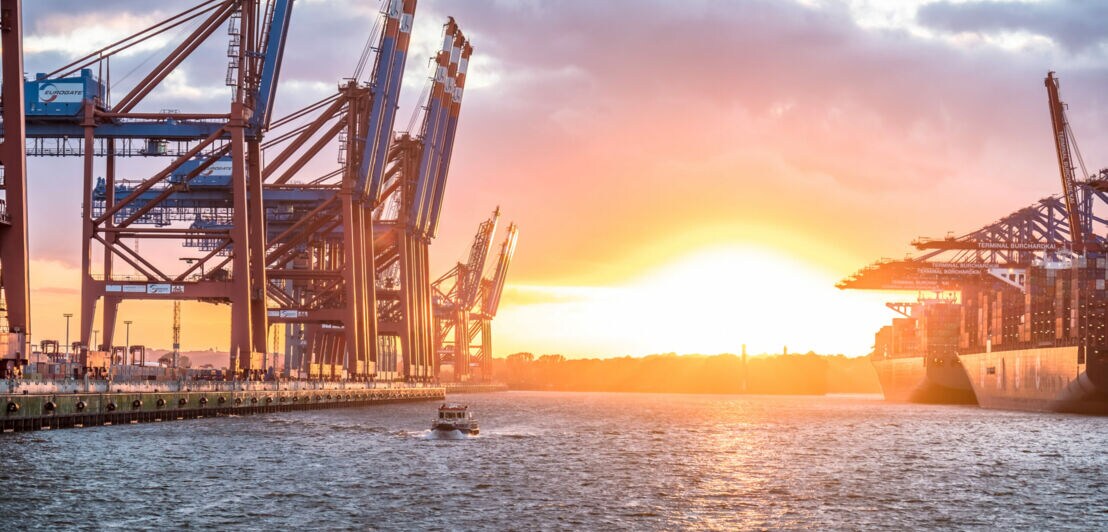 Sonnenuntergang über dem Waltershofer Hafen mit großen Containerkränen und einem Schiff im Wasser.