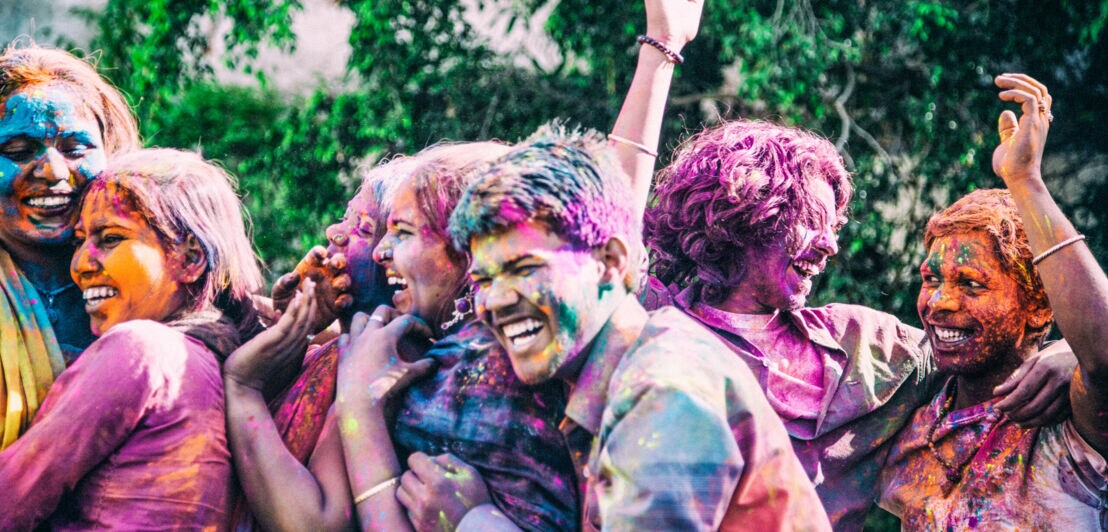 Lachende Personen, voll mit bunter Farbe, auf einem Holi Festival.