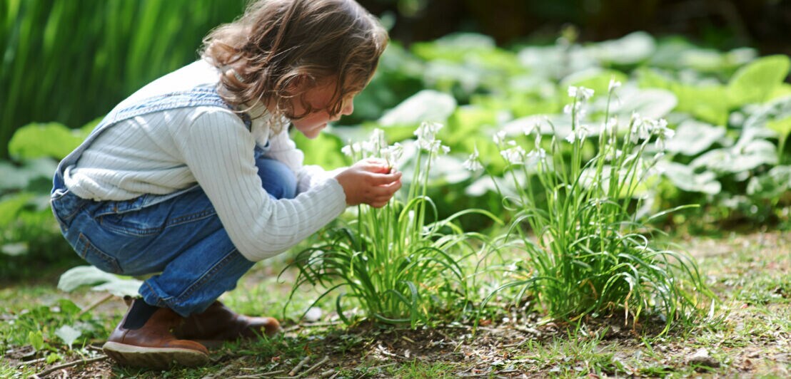 Ein Mädchen kniet und riecht an Blumen.