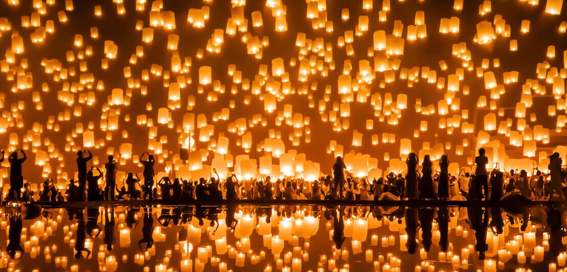 Unkenntliche Personen, die gleichzeitig im Dunkeln unzählige leuchtende Laternen in den Himmel steigen lassen.