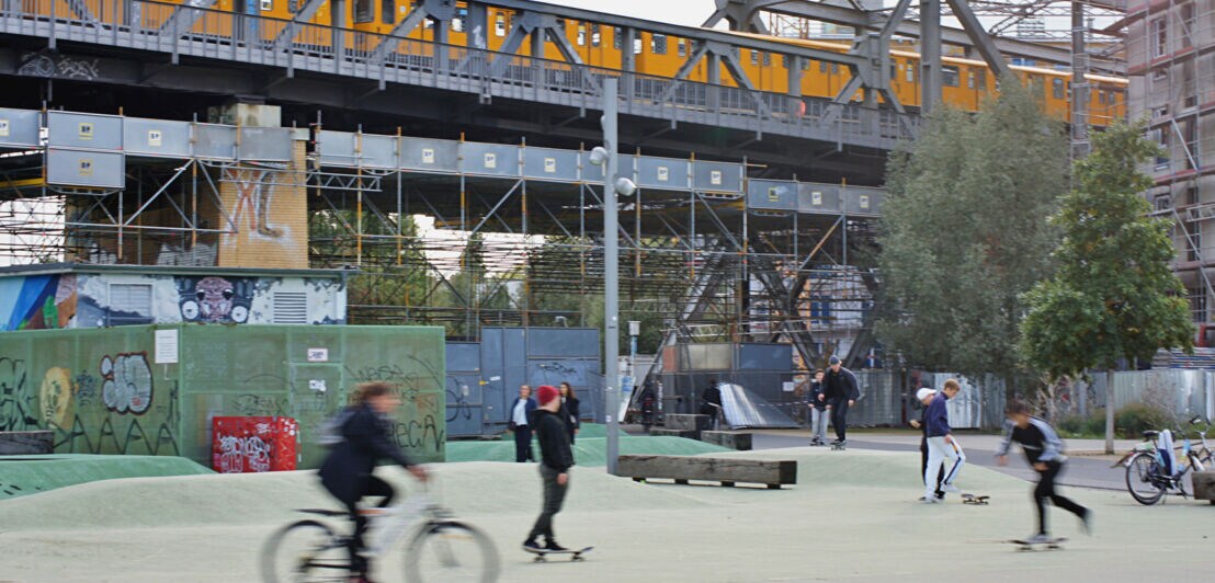 Jugendliche fahren Fahrrad und Skateboard auf einem Skaterplatz im Park am Gleisdreieck.
