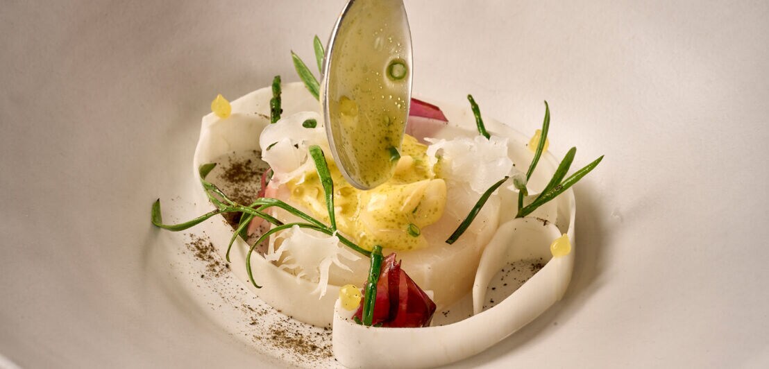 Ein stilvoll angerichtetes Fischgericht mit heller Soße auf einem weißen Teller.