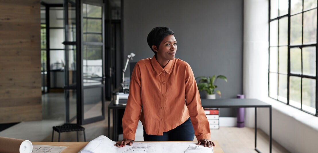 Eine Architektin steht konzentriert einem Tisch mit Bauplänen.