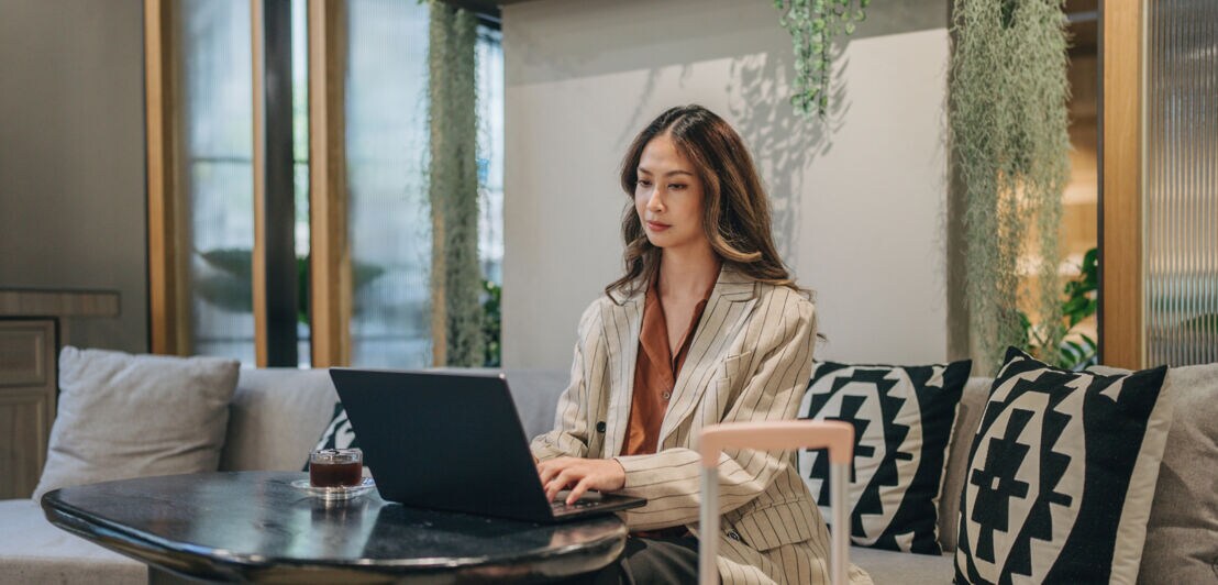 Eine Geschäftsfrau arbeitet in einer Hotellobby am Laptop.