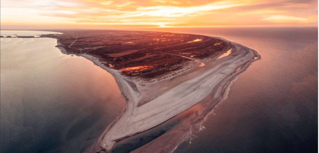 Luftaufnahme einer Sandbank und Küstenlinie bei Sonnenuntergang mit orangefarbenem Himmel und ruhigem Meer.