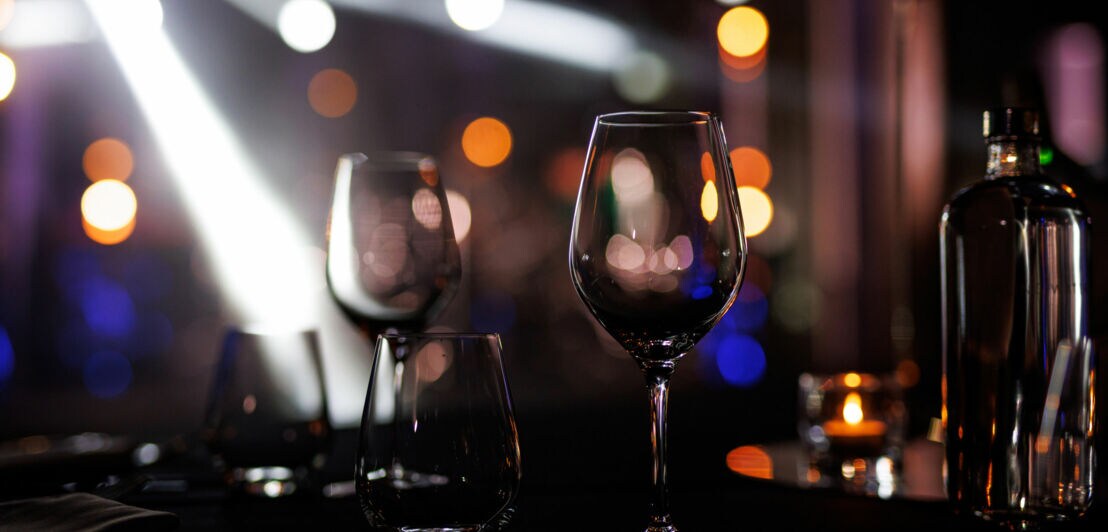 Leere Weingläser und eine Flasche auf einem Tisch vor unscharfem Hintergrund mit Lichtern