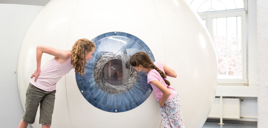 Zwei Mädchen blicken neugierig in ein großes, begehbares Modell eines menschlichen Auges im Museum EXPERIMINTA