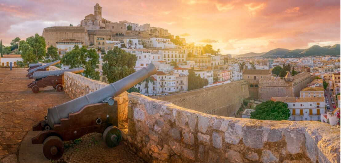 Historische Kanonen auf einer Steinmauer mit Blick auf die Altstadt von Ibiza bei Sonnenuntergang
