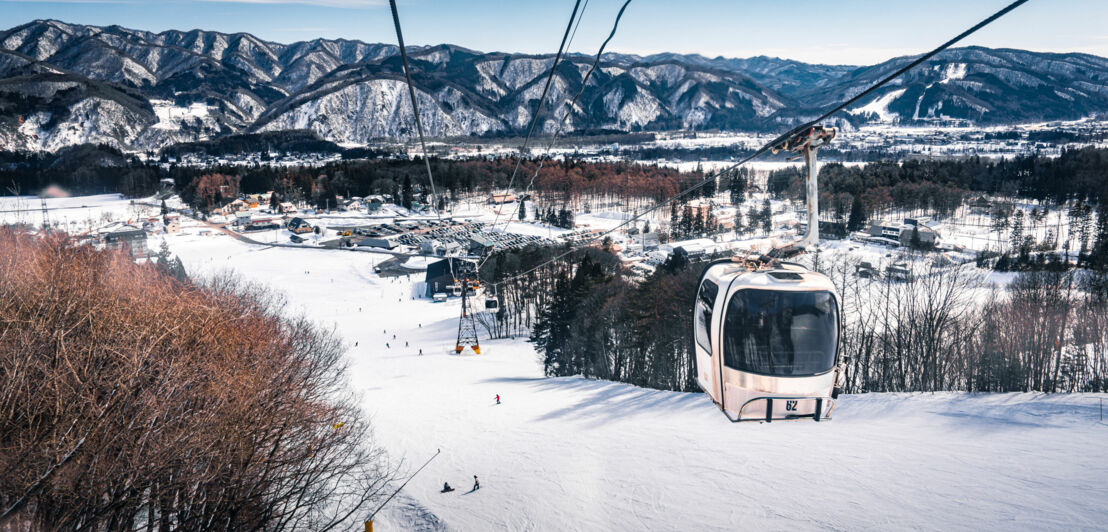 Blick von einem Sessellift auf ein schneebedecktes Skigebiet mit Skifahrern und Bergen im Hintergrund