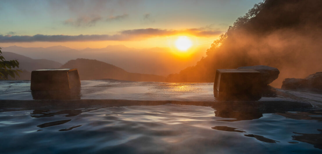 Sonnenuntergang über nebligen Bergen mit Blick auf einen Infinity-Pool im Vordergrund