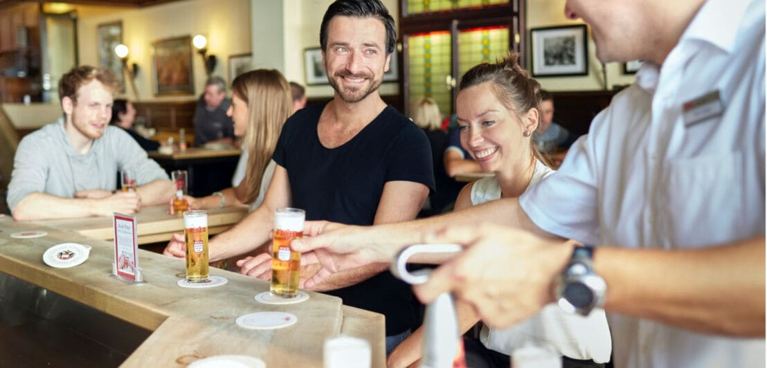 Mehrere Personen sitzen an einer Bar im Früh Brauhaus und erhalten Gläser mit Kölsch-Bier vom Kellner.