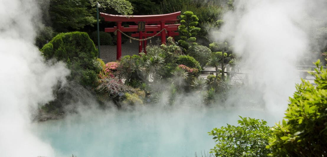 Dampfende Thermalquelle in einem japanischen Garten mit rotem Shintō-Schrein.
