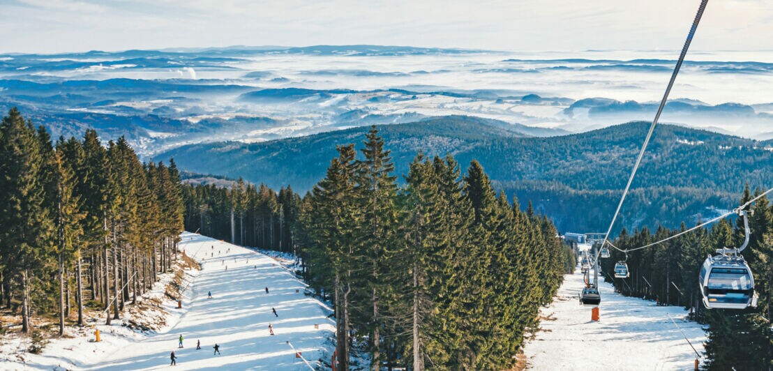Eine Piste mit Skifahrern und Skilift zwischen Wäldern.