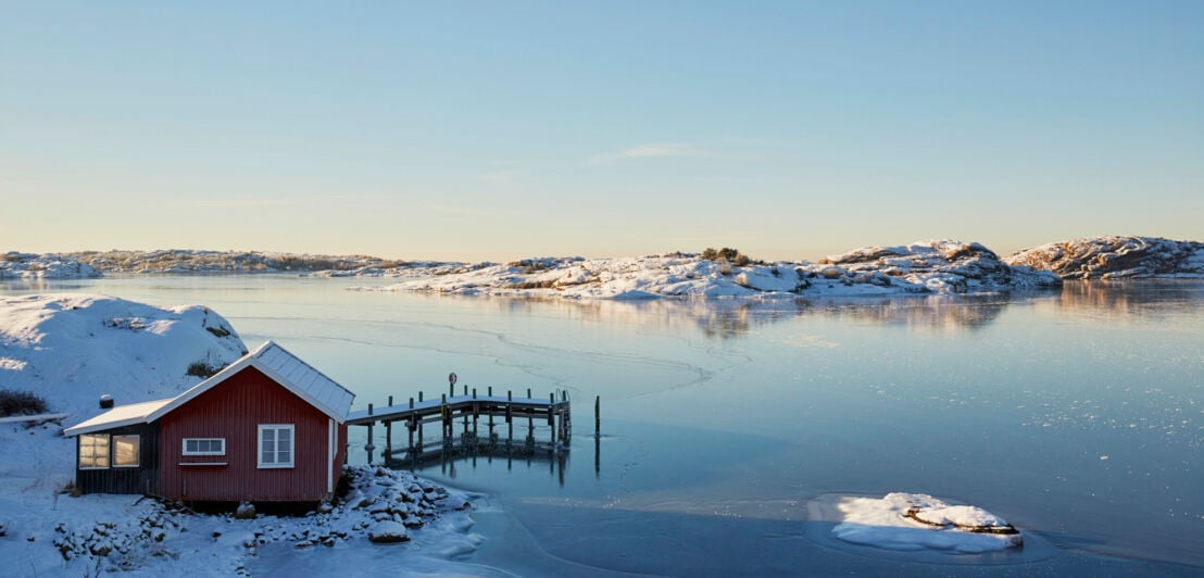 Rote schwedische Hütte, die in einer Winterlandschaft am See steht.